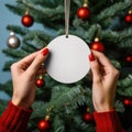 female hands holding white blank christmas ball on tree background, AI Generated Royalty Free Stock Photo