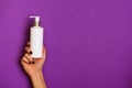 Female hands holding white cosmetic bottle on violet background. Banner. Skin care, pure beauty, body treatment concept
