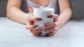 Female hands are holding a white cup of coffee on a light wooden table. The concept of suffering, despair, problems