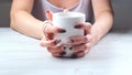 Female hands are holding a white cup of coffee on a light wooden table. The concept of suffering, despair, problems