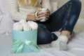 Female hands holding a white mug with latte coffee . Marshmallows amd meringues in a box. Life style concept. Close up Royalty Free Stock Photo