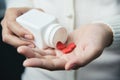 Female hands is holding a white pill bottle and red pills in heart shape. Royalty Free Stock Photo