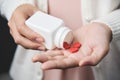 Female hands is holding a white pill bottle and red pills in heart shape. Royalty Free Stock Photo