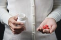 Female hands is holding a white pill bottle and red pills in heart shape. Royalty Free Stock Photo