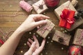 Female hands holding, wrapping Christmas gift box. Group of gift boxes wraped in craft paper, red baubles, glitter over wooden Royalty Free Stock Photo