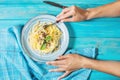 Female hands holds a fork. Pasta with chanterelle mushroom and ingredients on blue wooden background.