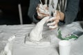 Female hands with an instrument gracefully shape a small plaster sculpture.