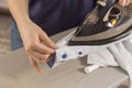 Female hands iron the shirt sleeve on a stand on an ironing board. Ironed clothes lie on the table in the background.