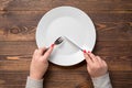 Female hands with knife and fork over white empty plate. Wooden table Royalty Free Stock Photo