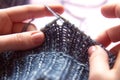 Female hands with knitting needles to knit wool blue sweater on pink background