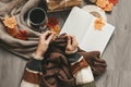 Female hands knitting sweater on the floor with autumn leaves and cup of coffee