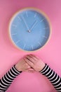 Female hands and large clock on pink background