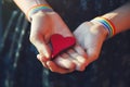 Female hands with LGBT colorful rainbow ribbon wristbands holding red wooden heart Royalty Free Stock Photo