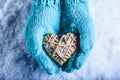 Female hands in light teal knitted mittens with entwined beige flaxen heart on a white snow background. St. Valentines Day concept Royalty Free Stock Photo