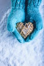 Female hands in light teal knitted mittens with entwined beige flaxen heart on a white snow background. St. Valentines Day concept Royalty Free Stock Photo