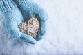 Female hands in light teal knitted mittens with entwined beige flaxen heart on a white snow. Love, St. Valentines Day concept