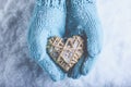 Female hands in light teal knitted mittens with entwined beige flaxen heart on a white snow. Love, St. Valentines Day concept Royalty Free Stock Photo