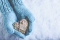 Female hands in light teal knitted mittens with entwined beige flaxen heart on a white snow. Love, St. Valentines Day concept Royalty Free Stock Photo