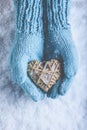 Female hands in light teal knitted mittens with entwined beige flaxen heart on a white snow. Love, St. Valentines Day concept