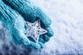 Female hands in light teal knitted mittens with entwined white star on a white snow background. Winter and Christmas concept. Royalty Free Stock Photo