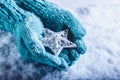 Female hands in light teal knitted mittens with entwined white star on a white snow background. Winter and Christmas concept. Royalty Free Stock Photo