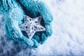 Female hands in light teal knitted mittens with entwined white star on a white snow background. Winter and Christmas concept. Royalty Free Stock Photo