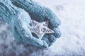 Female hands in light teal knitted mittens with entwined white star on a white snow background. Winter and Christmas concept. Royalty Free Stock Photo