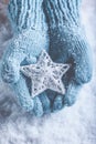 Female hands in light teal knitted mittens with entwined white star on a white snow background. Winter and Christmas concept. Royalty Free Stock Photo