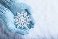 Female hands in light teal knitted mittens with sparkling wonderful snowflake on snow background. Winter and Christmas concept Royalty Free Stock Photo