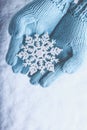 Female hands in light teal knitted mittens with sparkling wonderful snowflake on snow background. Winter and Christmas concept Royalty Free Stock Photo