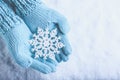 Female hands in light teal knitted mittens with sparkling wonderful snowflake on snow background. Winter and Christmas concept Royalty Free Stock Photo