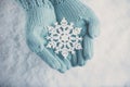 Female hands in light teal knitted mittens with sparkling wonderful snowflake on white snow background. Winter, Christmas concept Royalty Free Stock Photo