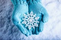 Female hands in light teal knitted mittens with sparkling wonderful snowflake on a white snow background. Winter Christmas concept