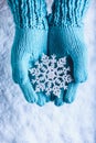 Female hands in light teal knitted mittens with sparkling wonderful snowflake on a white snow background. Winter Christmas concept