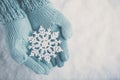 Female hands in light teal knitted mittens with sparkling wonderful snowflake on white snow background. Winter, Christmas concept Royalty Free Stock Photo