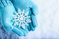 Female hands in light teal knitted mittens with sparkling wonderful snowflake on a white snow background. Winter Christmas concept Royalty Free Stock Photo