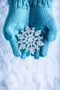 Female hands in light teal knitted mittens with sparkling wonderful snowflake on a white snow background. Winter Christmas concept Royalty Free Stock Photo