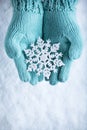 Female hands in light teal knitted mittens with sparkling wonderful snowflake on white snow background. Winter, Christmas concept Royalty Free Stock Photo