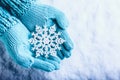 Female hands in light teal knitted mittens with sparkling wonderful snowflake on a white snow background. Winter Christmas concept