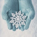 Female hands in light teal knitted mittens with sparkling wonderful snowflake on white snow background. Winter, Christmas concept Royalty Free Stock Photo