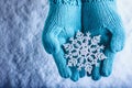 Female hands in light teal knitted mittens with sparkling wonderful snowflake on a white snow background. Winter Christmas concept Royalty Free Stock Photo