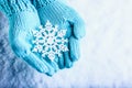 Female hands in light teal knitted mittens with sparkling wonderful snowflake on a white snow background. Winter Christmas concept Royalty Free Stock Photo