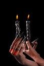 Female hands with long nails hold burning candles on a black background. concept of witchcraft witchcraft on halloween.
