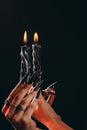 Female hands with long nails hold burning candles on a black isolated background. concept of witchcraft witchcraft on halloween.