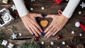 Female hands making a heart shape around a holiday cookie placed in the middle of christmas setting