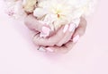 Female hands manicure flower peony on a pink background