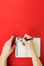 Female hands with manicure in green sweater write in notebook wish list, goals or promises for New Year on red