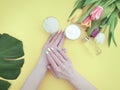 Female hands manicure, tulip flower  cosmetic hygiene essence creative cream summer , monstera leaf on a paper colored background Royalty Free Stock Photo