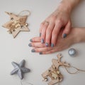 Female hands with Merry Christmas reindeer manicure on finger nails. White background with silver and wooden toys around.