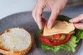 Female hands meticulously placing a slice of cheese atop a burger